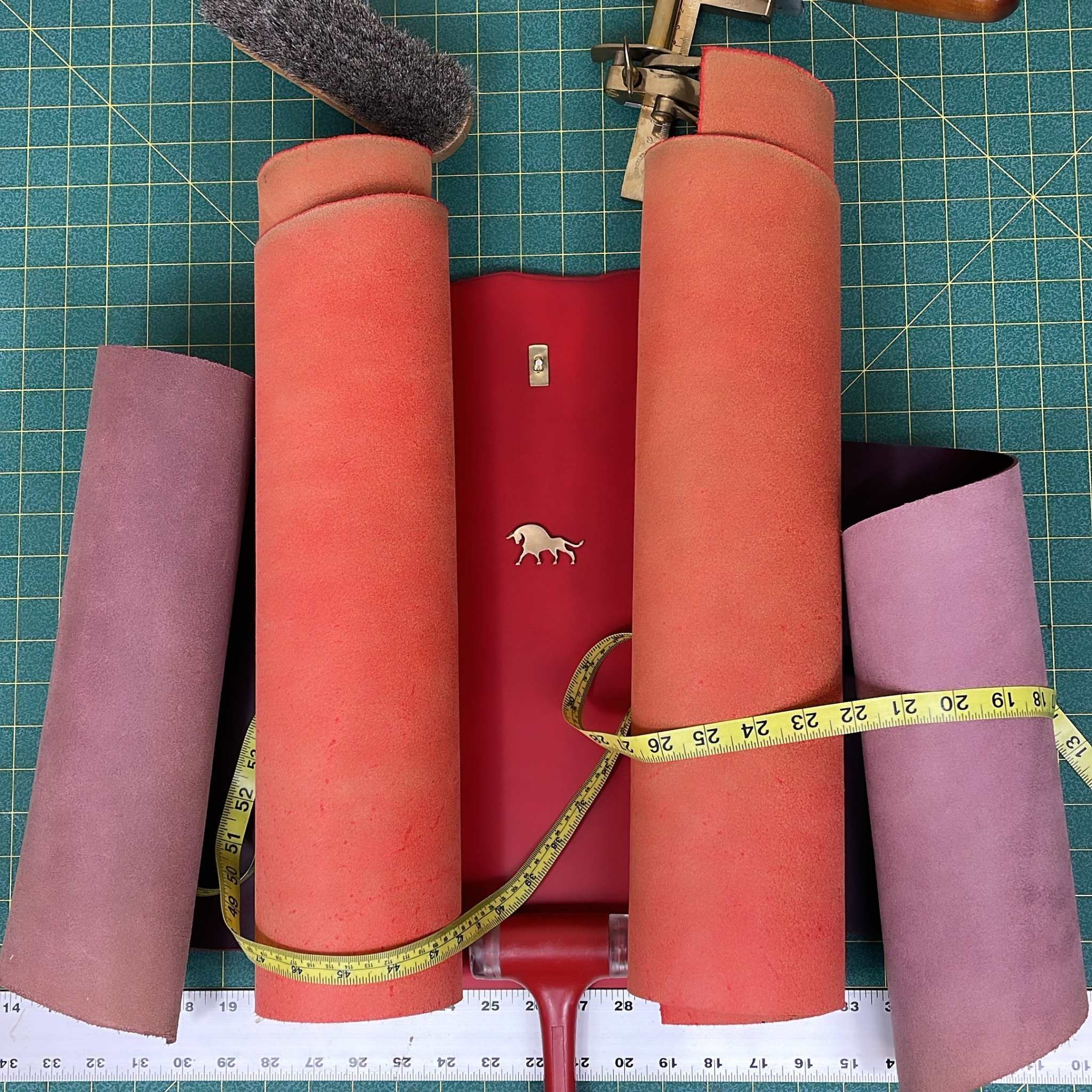 handmade leather belt materials rolled on a green cutting mat with measuring tape and leathercraft tools