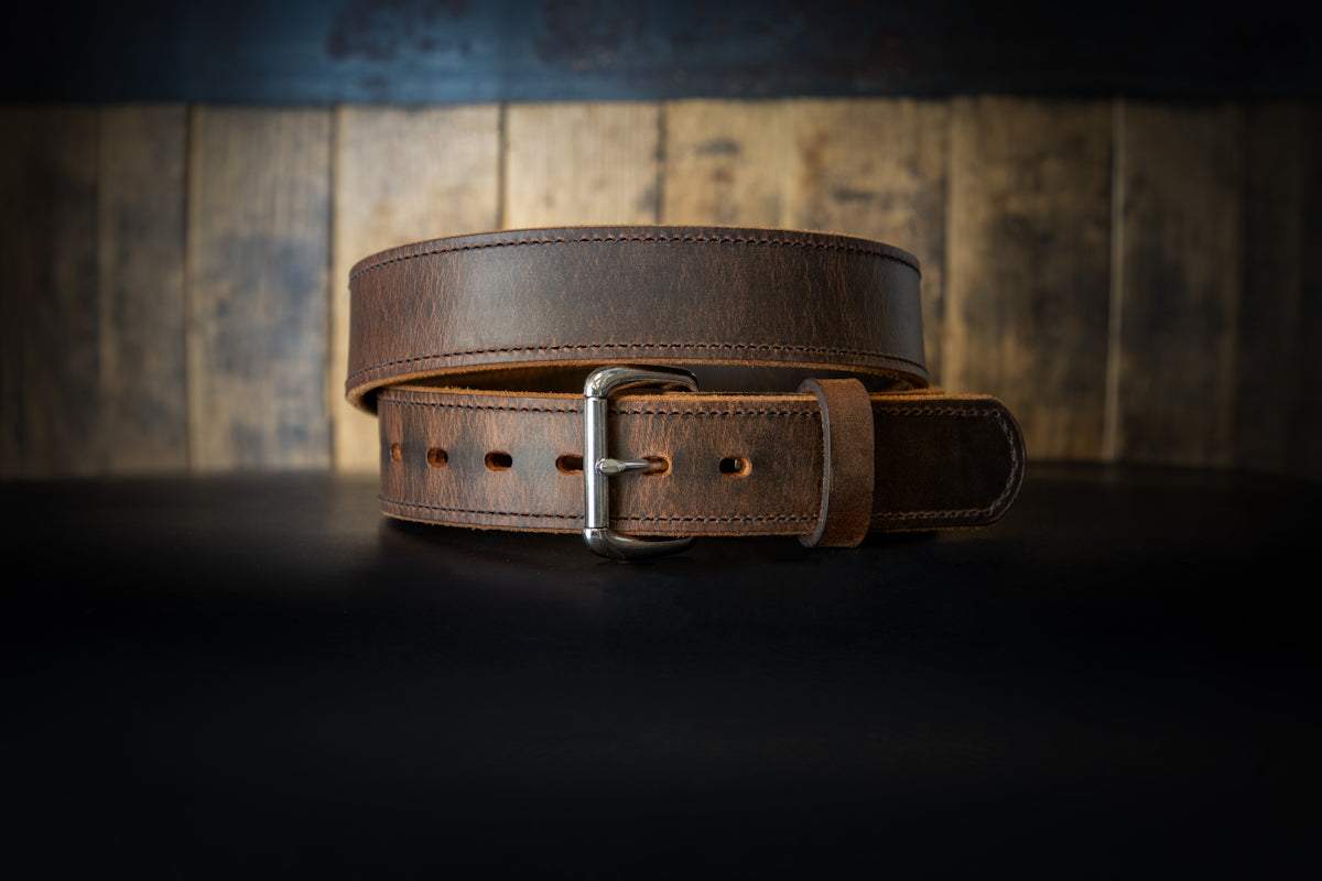 Brown men's leather belt with silver buckle on dark wooden background