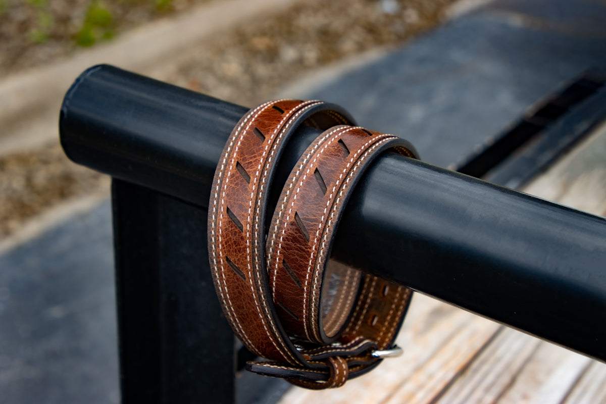 Handmade men's leather belts wrapped on black metal railing outdoors