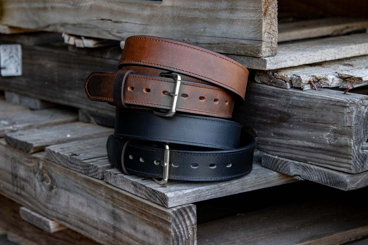 Two men's premium leather belts, brown and black, rolled and placed on wooden surface