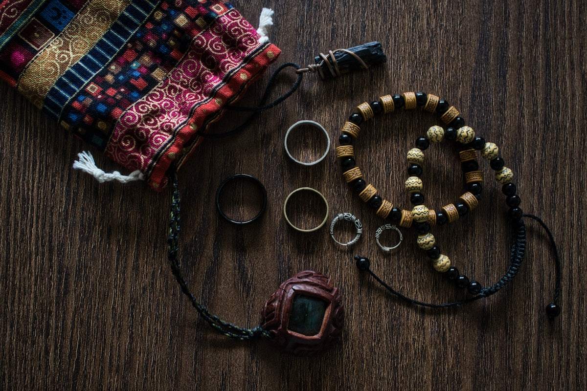 men’s handmade accessories including beaded bracelets, rings, leather necklace, and patterned fabric pouch on wooden surface
