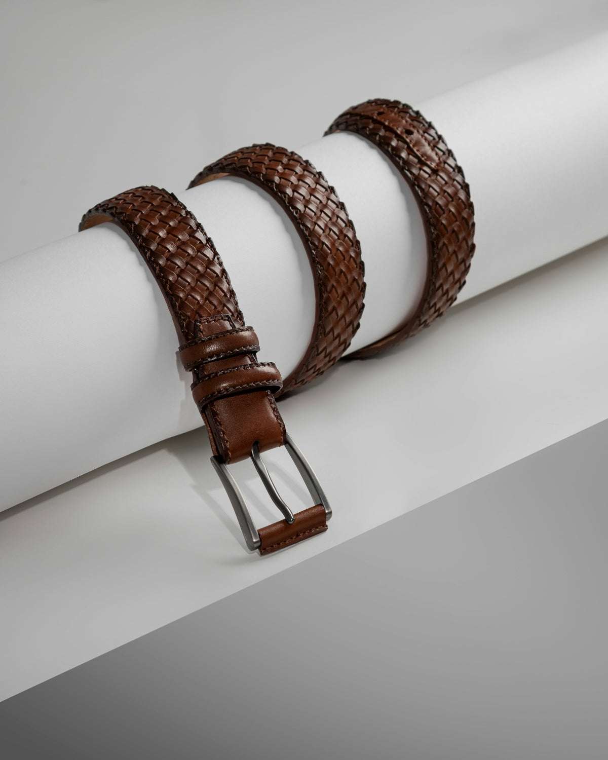 brown woven leather men's formal belt with silver buckle arranged on white surface