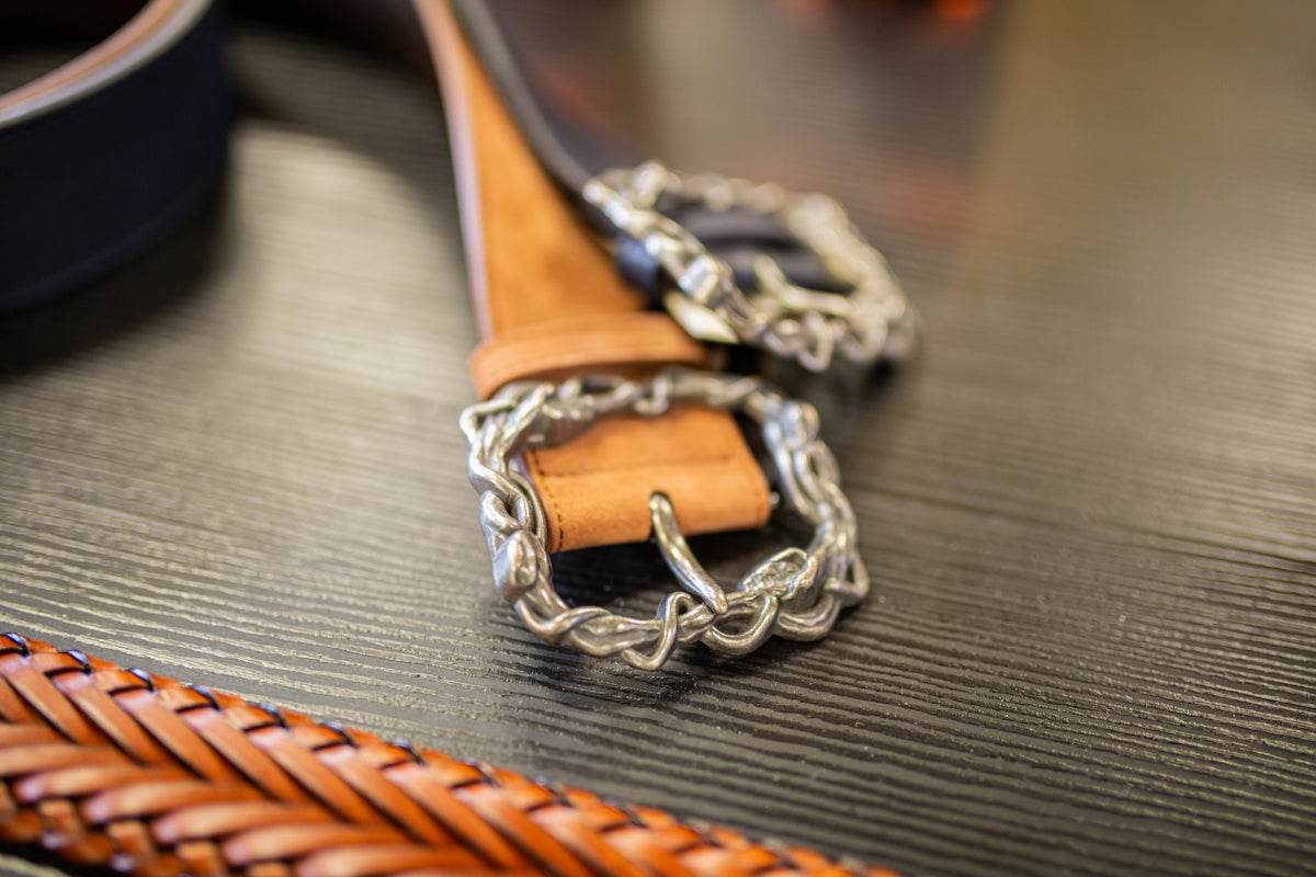 Two men's formal leather belts with decorative silver buckles on a wooden surface