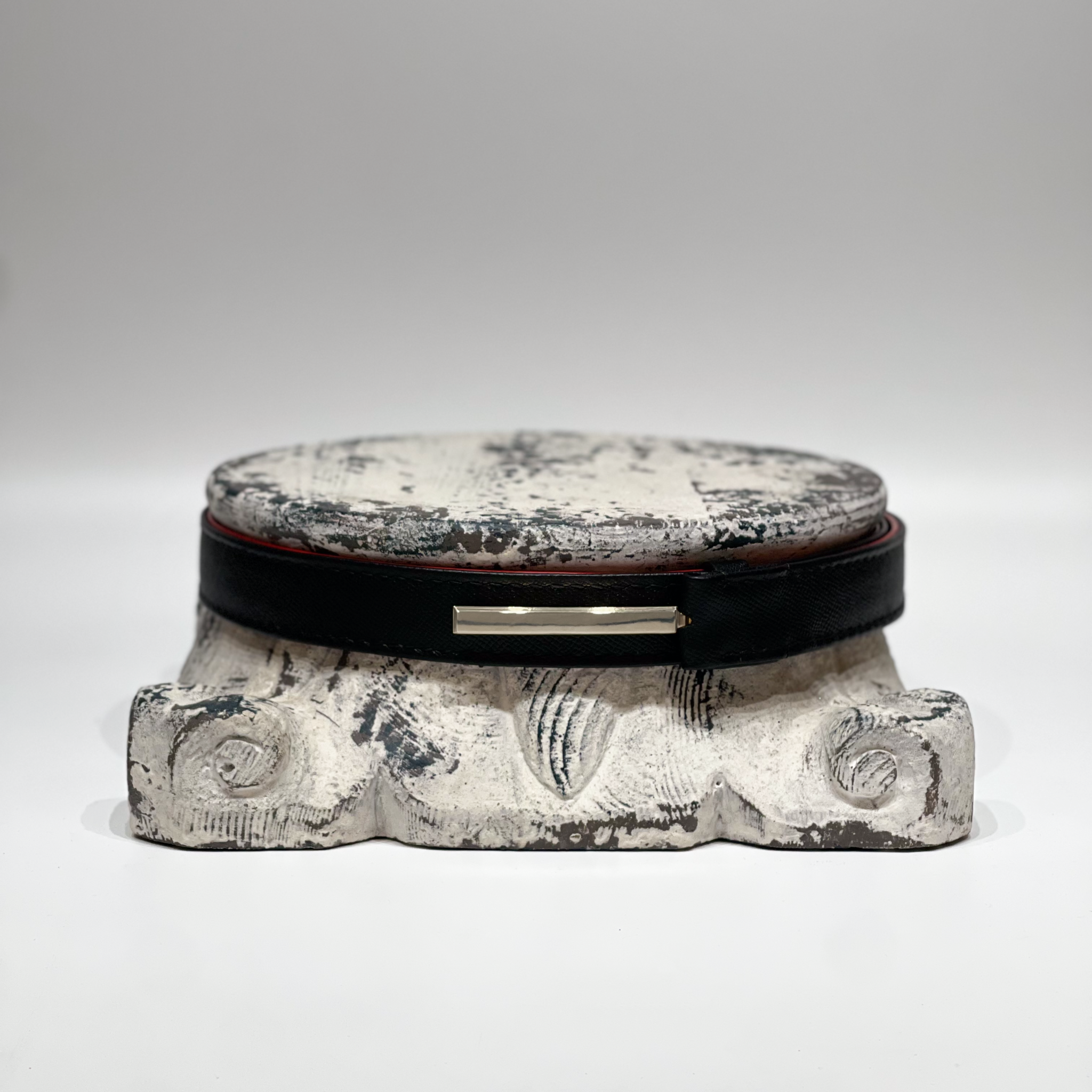 Handmade Domus Belt in black full grain leather with platinum-plated buckle displayed on rustic stone pedestal